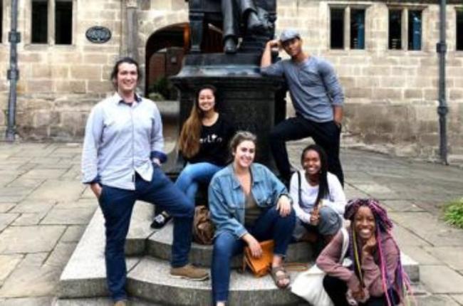 A group of students sit on a statue and pose for a picture.