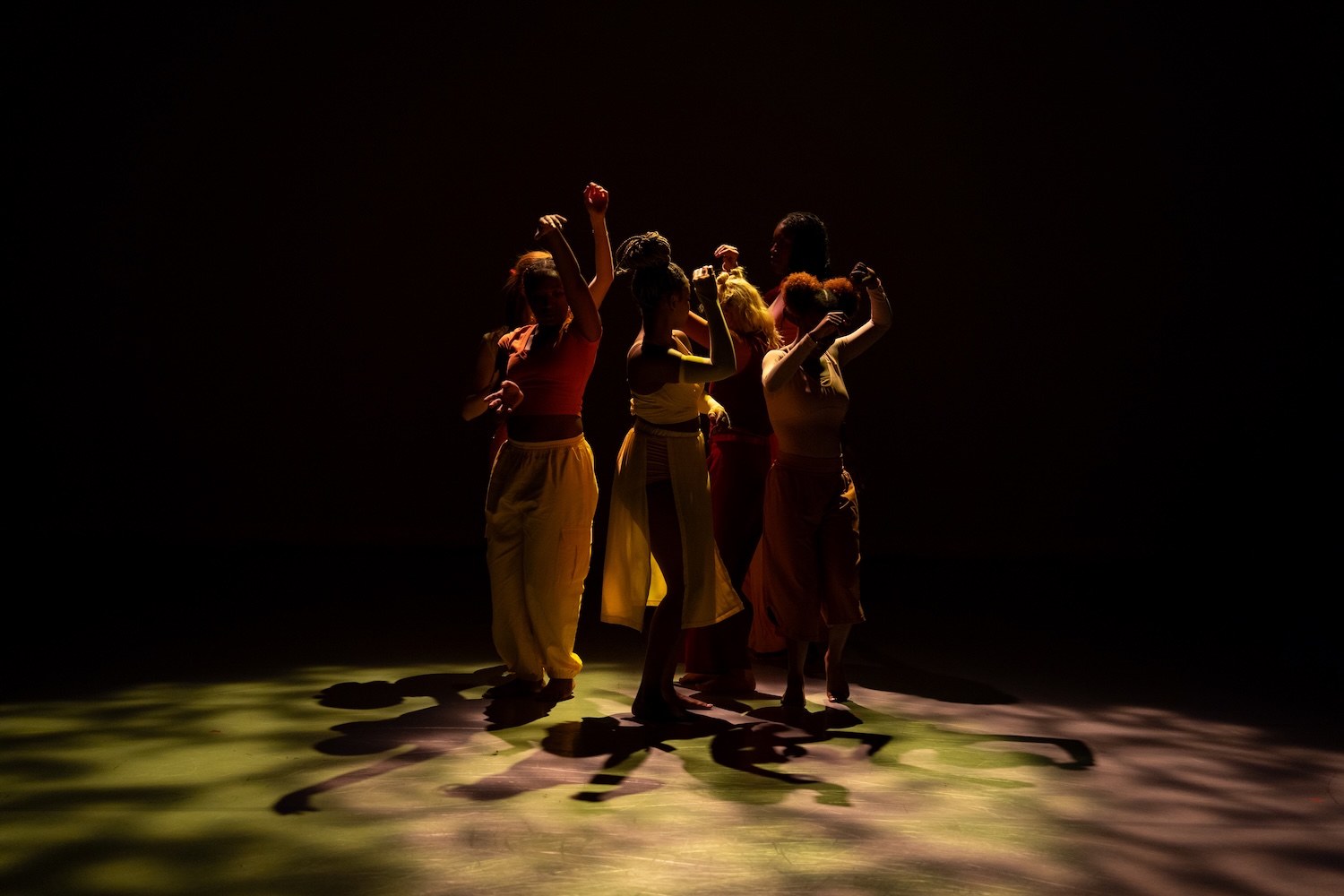 A group of dancers perform on a darkened stage.