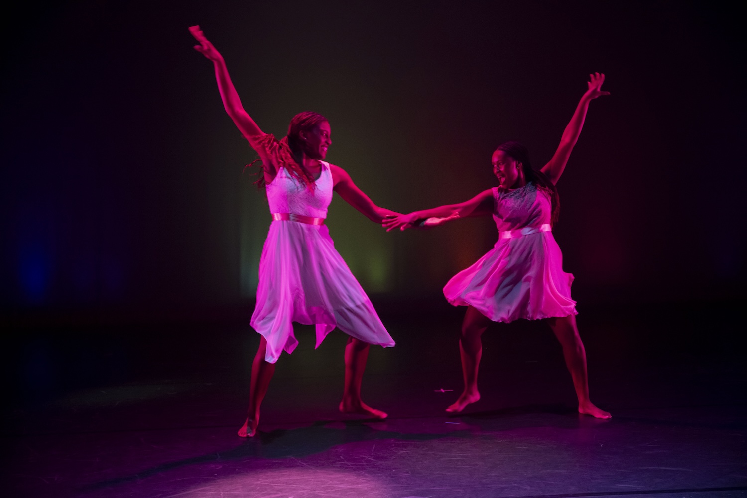 Two dancers reach toward each other on a dark stage with vibrant lighting.