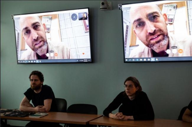 Two people sit in a classroom being shared on Zoom.