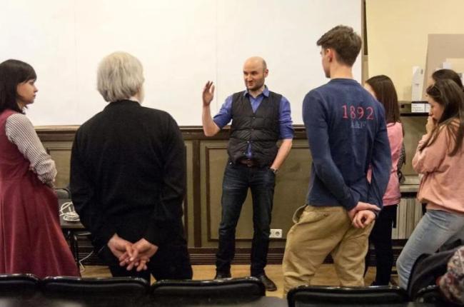 A man speaks to a small group of people in a lecture hall.