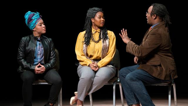 Three Black people talk while sitting on stools on stage.