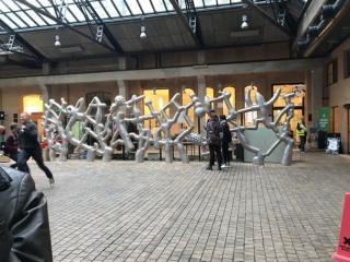 People look at a large metal sculpture in a courtyard.